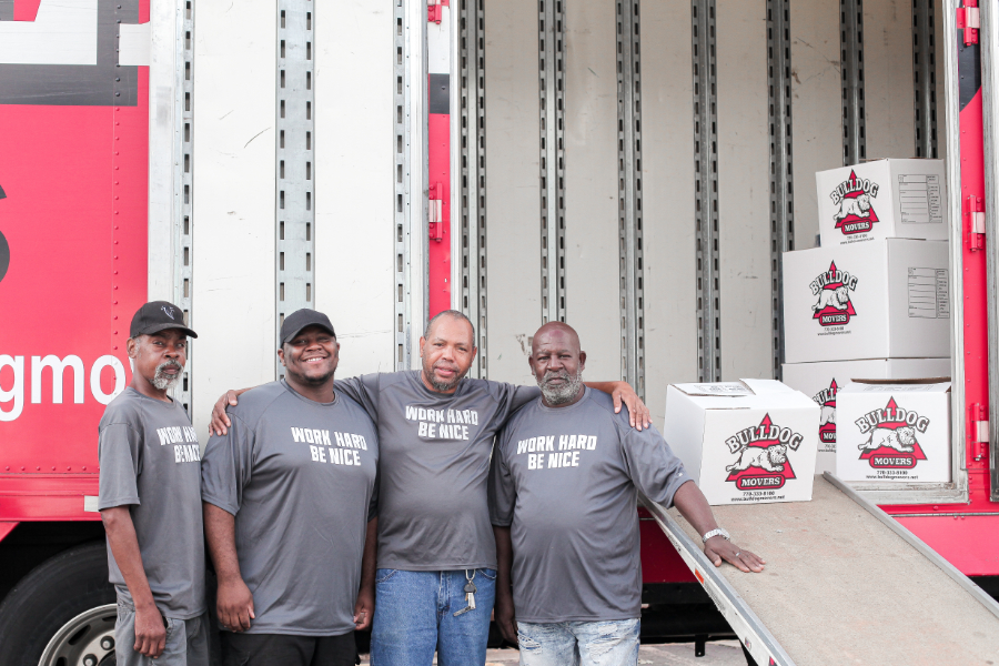 Four men posing next to moving truck ramp