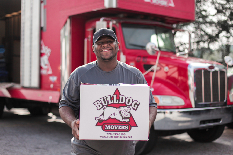 Man smiling holding box in front of moving truck